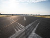 an empty runway with three long lines in the middle of it, and sun on either side