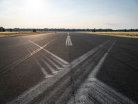 an empty runway with three long lines in the middle of it, and sun on either side