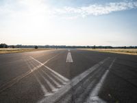 an empty runway with three long lines in the middle of it, and sun on either side