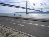 two motorcyclists driving next to the sea under a bridge in spain on a sunny day