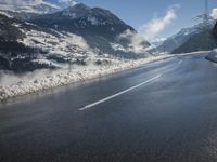 a road on a sunny day with snowy mountains in the background, surrounded by snow and clouds