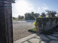 looking out the front door of a house into an area of gravel and vegetation, with sunlight shining through