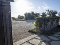 looking out the front door of a house into an area of gravel and vegetation, with sunlight shining through