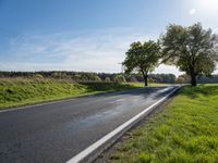 an empty road is lined with grassy meadows and trees in the sun near a park