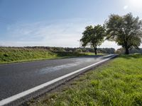 an empty road is lined with grassy meadows and trees in the sun near a park