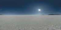 the sun in the blue sky above some sand and desert hills and trees and hill with a clear sky