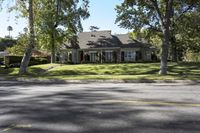 a home sitting next to a street lined with trees and shrubs on a nice day