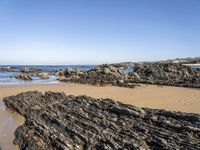 a sandy beach with small rocks and water on the shore at low tide, on sunny day