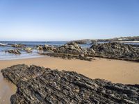 a sandy beach with small rocks and water on the shore at low tide, on sunny day