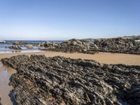 a sandy beach with small rocks and water on the shore at low tide, on sunny day