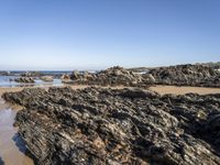 a sandy beach with small rocks and water on the shore at low tide, on sunny day