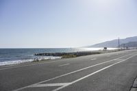 a highway that is lined with white lines to show the ocean and beach area in the background