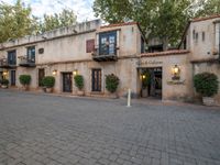 a restaurant with an attached entrance is near the street and trees and flowers in pots