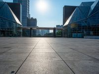 a large, empty courtyard in the middle of some tall buildings with a bright sun shining out