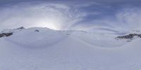 this picture shows snow skiiers on a sunny day in the mountains with large circular clouds