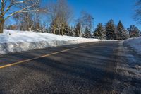 a snow covered road is surrounded by trees and snow - covered mountains in the distance