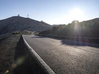 the sun shining on the road between two mountains in an arid landscape with no clouds