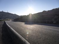 the sun shining on the road between two mountains in an arid landscape with no clouds