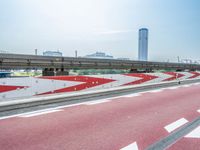 a very long red and white bridge spanning over an empty highway area with buildings in the background