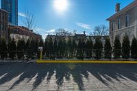 a yellow barrier on a paved pavement surrounded by trees and bushes and blue sky with the sun shining behind it