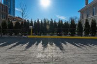 a yellow barrier on a paved pavement surrounded by trees and bushes and blue sky with the sun shining behind it