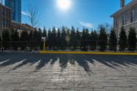 a yellow barrier on a paved pavement surrounded by trees and bushes and blue sky with the sun shining behind it