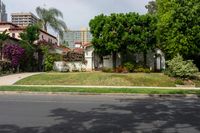 a house with green trees around the front yard and green grass surrounding it and buildings