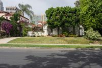 a house with green trees around the front yard and green grass surrounding it and buildings