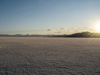 the sun is shining behind mountains in the desert land with white snow in front of the mountain range