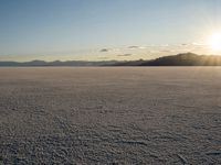 the sun is shining behind mountains in the desert land with white snow in front of the mountain range