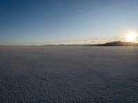 the sun is shining behind mountains in the desert land with white snow in front of the mountain range