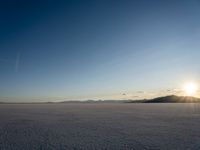 the sun is shining behind mountains in the desert land with white snow in front of the mountain range