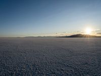 the sun is shining behind mountains in the desert land with white snow in front of the mountain range