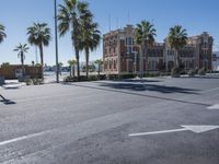 the sun shines behind palm trees on an empty street with buildings and a park