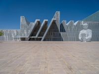 a white building with several steps and large glass panels in the facade is a mosaic that depicts a man