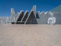 a white building with several steps and large glass panels in the facade is a mosaic that depicts a man