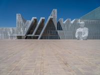 a white building with several steps and large glass panels in the facade is a mosaic that depicts a man