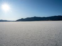 some type of desert with mountains in the background and sunlight casting shadows all over the sand