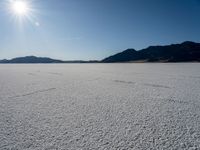 some type of desert with mountains in the background and sunlight casting shadows all over the sand