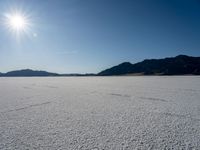 some type of desert with mountains in the background and sunlight casting shadows all over the sand