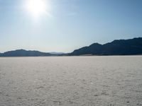 some type of desert with mountains in the background and sunlight casting shadows all over the sand