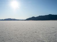 some type of desert with mountains in the background and sunlight casting shadows all over the sand