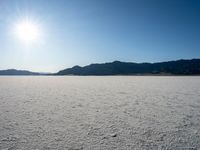 some type of desert with mountains in the background and sunlight casting shadows all over the sand