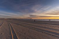 people walking down a beach towards the ocean at sunset while on a sunny day with tracks in the sand