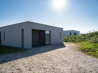 small house with flat roof sitting on grass field next to building with sliding glass doors