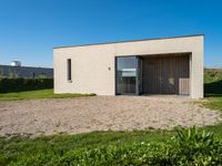 small house with flat roof sitting on grass field next to building with sliding glass doors