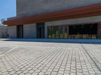 a brick paved area in front of a building with wooden chairs and tables on it