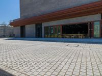 a brick paved area in front of a building with wooden chairs and tables on it