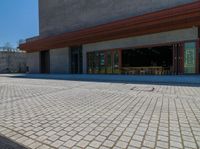 a brick paved area in front of a building with wooden chairs and tables on it