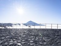 the sun is shining over a mountain in front of a fence with snow on top